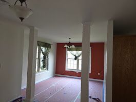 Interior view of a room with white columns, red walls, and a window with green curtains.