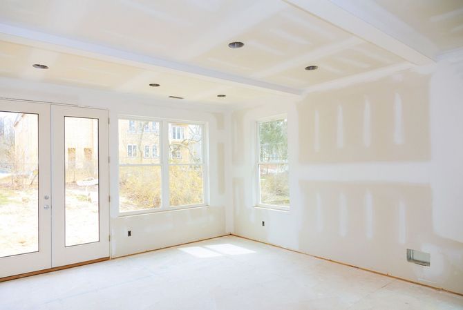 Interior of a room under construction, with drywall on walls and ceiling, windows and doors.