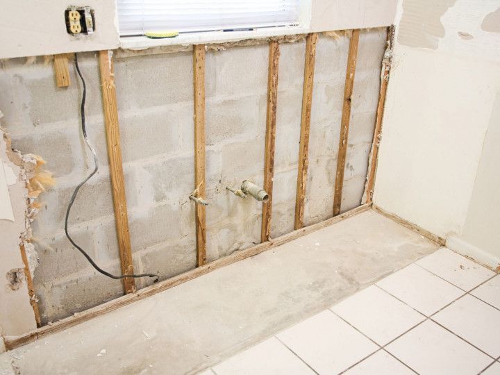Interior wall demolition in a kitchen, exposing cinder blocks, framing, and a drainpipe.