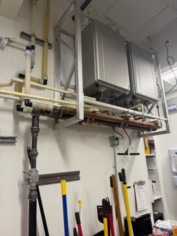 Industrial utility room with wall-mounted pipes, valves, and a large metal unit above cleaning tools