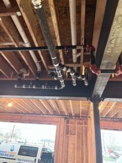 Exposed ceiling pipes and wooden beams inside a garage, with a white van parked below.