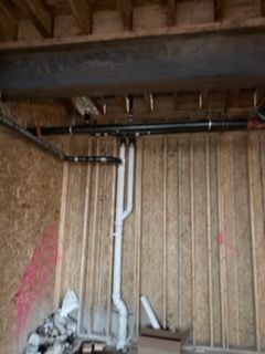 Basement wall with exposed plumbing pipes and beams, next to a pile of debris