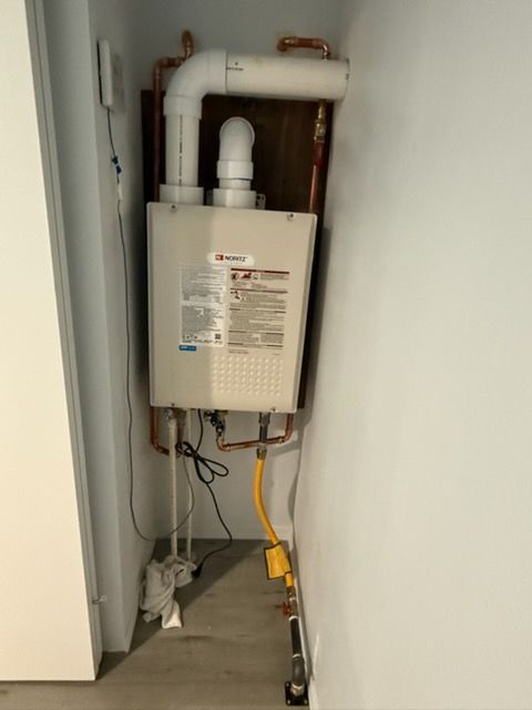 Wall-mounted white gas water heater with exposed pipes and yellow shutoff valve in a utility closet