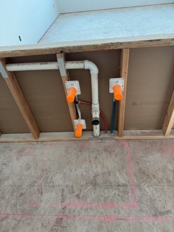 Plumbing pipes and orange-handled valves mounted under a counter or sink, with exposed wooden framing.