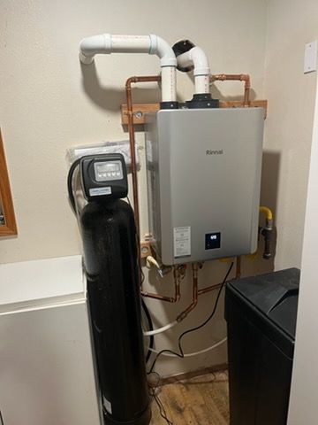 Water softener and wall-mounted tankless water heater in a utility room with exposed copper piping.