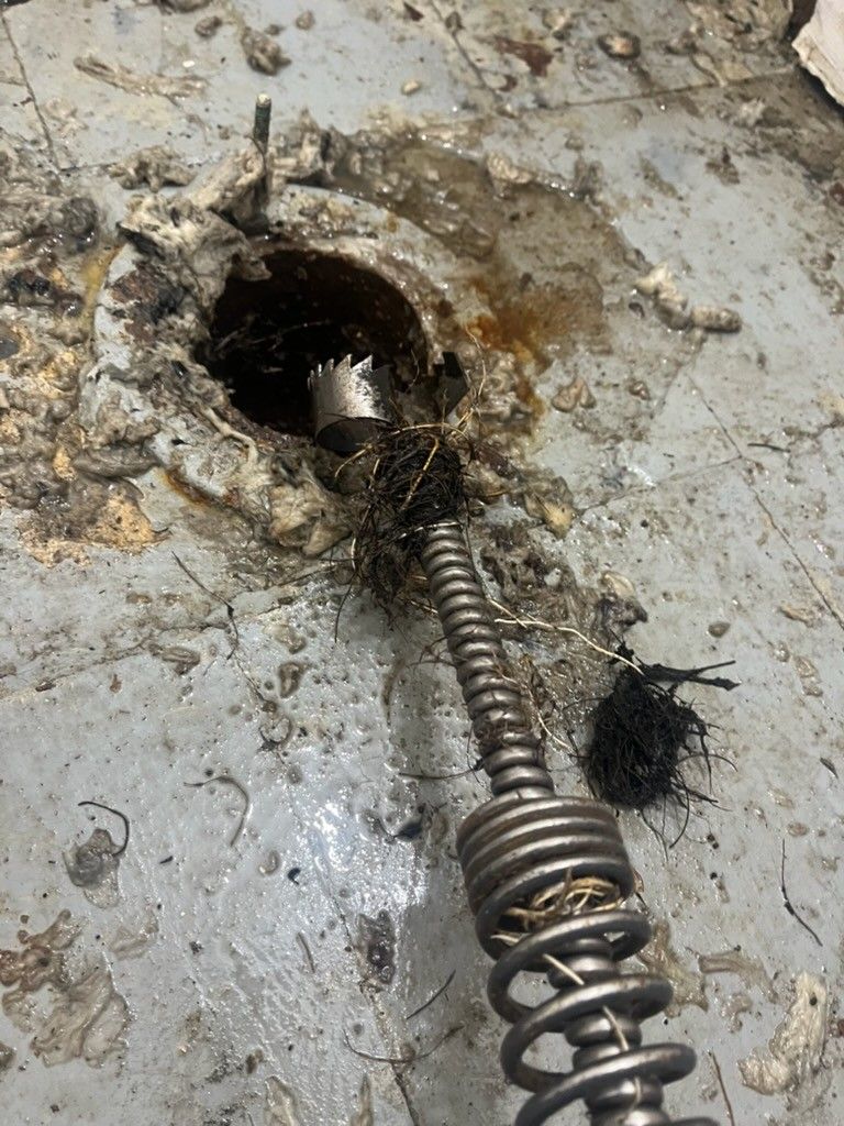 A plumber in a blue uniform, performing drain cleaning services, unclogging a kitchen sink.