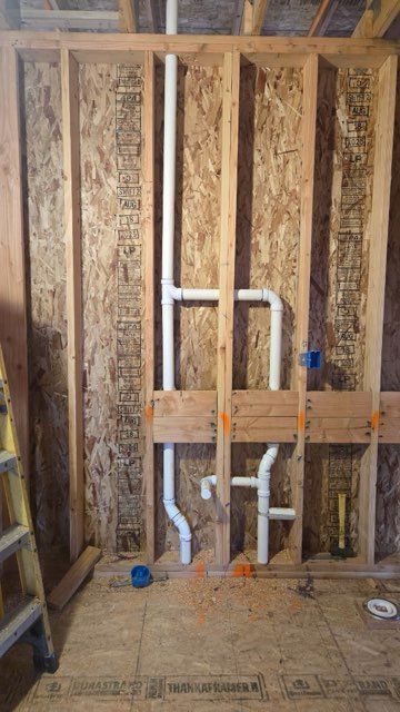 Framed bathroom plumbing wall with white PVC pipes and wood studs during construction