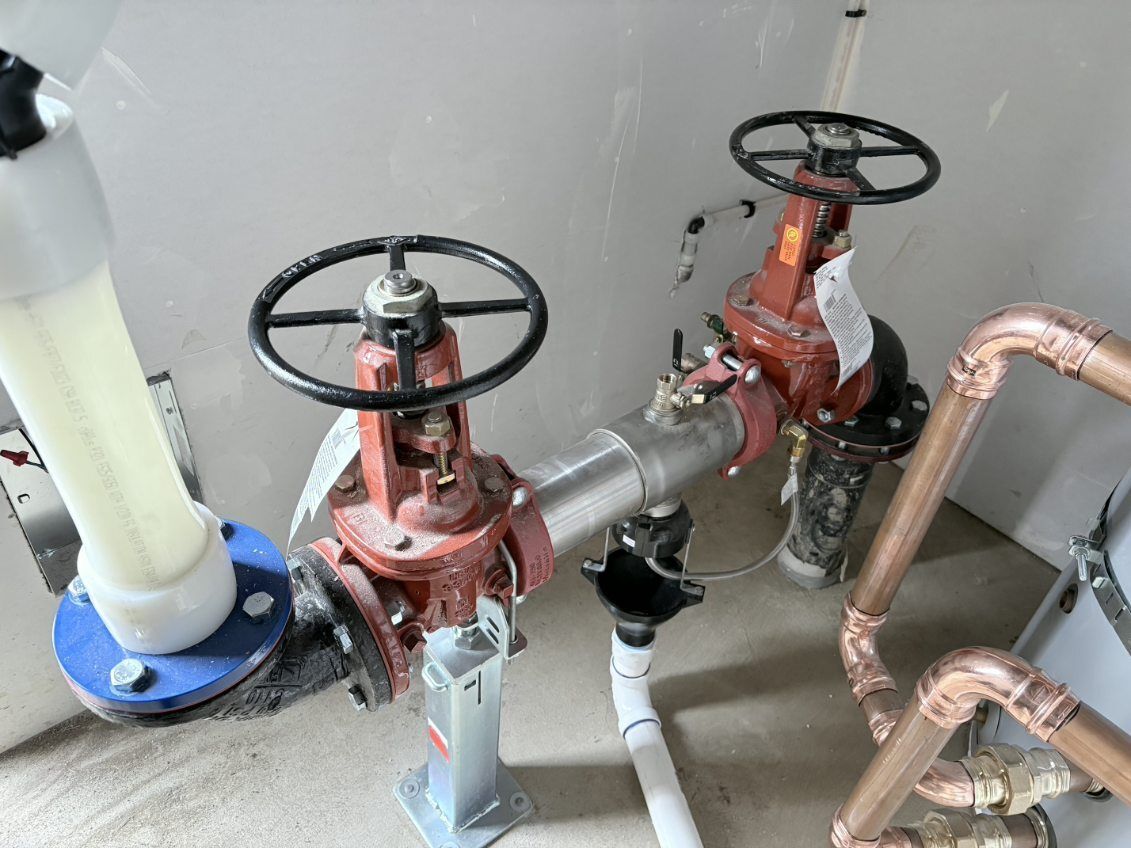 Industrial pipes and red valve wheels connected to metal piping in a utility room