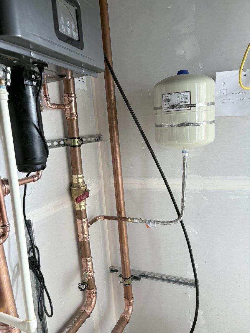 Boiler room pipes and a white expansion tank mounted on a wall, with plumbing fittings and valves.