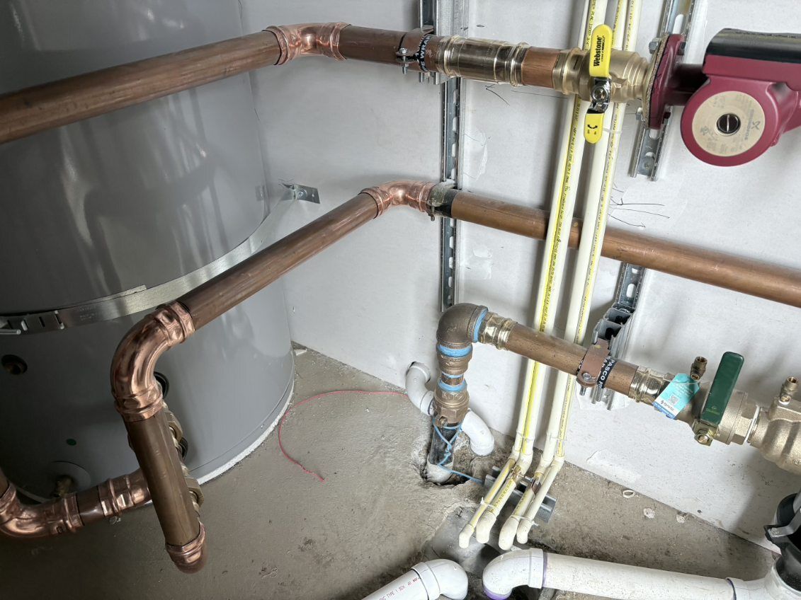 Copper and white plumbing pipes and valves along a basement wall near a water heater