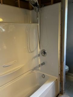 White bathtub with shower, chrome fixtures, inside a partially finished bathroom.