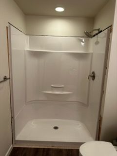 White, built-in shower stall with shelving and showerhead. Brown floor, toilet visible.