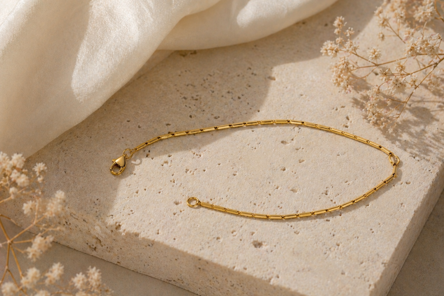 Collier à chaîne en or posé sur une surface en pierre beige, à côté d'un drapé de tissu crème.