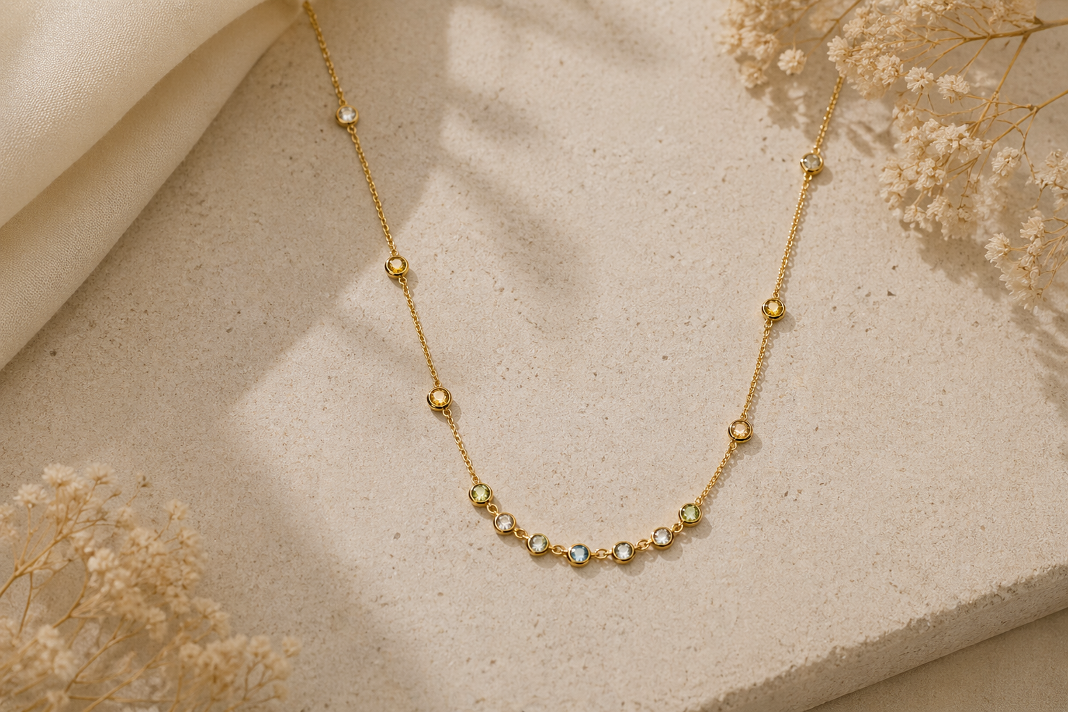 Collier en chaîne dorée avec petites perles présenté sur un tissu beige