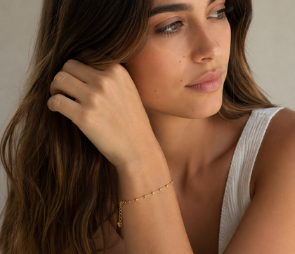 Portrait d'une femme aux longs cheveux bruns, vêtue d'un haut blanc et d'un bracelet en or, regardant sur le côté