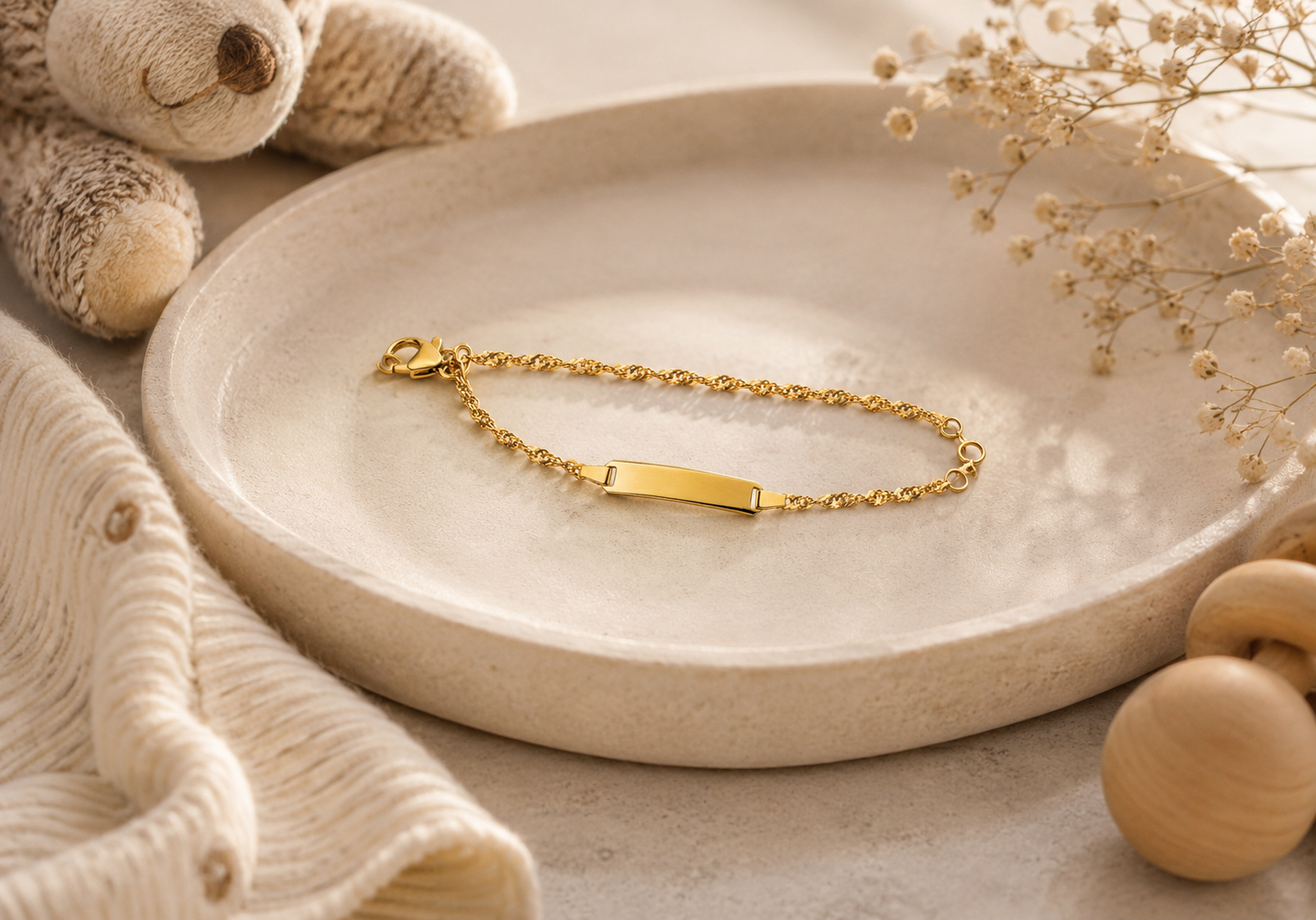 Bracelet en or posé sur un plat en céramique beige, le tout agrémenté d'un décor neutre et doux et de fleurs séchées.