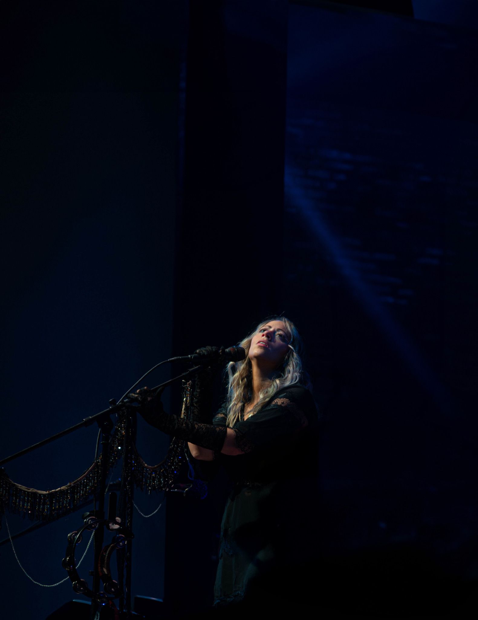 Singer on stage with microphone, dark blue setting, spotlight.