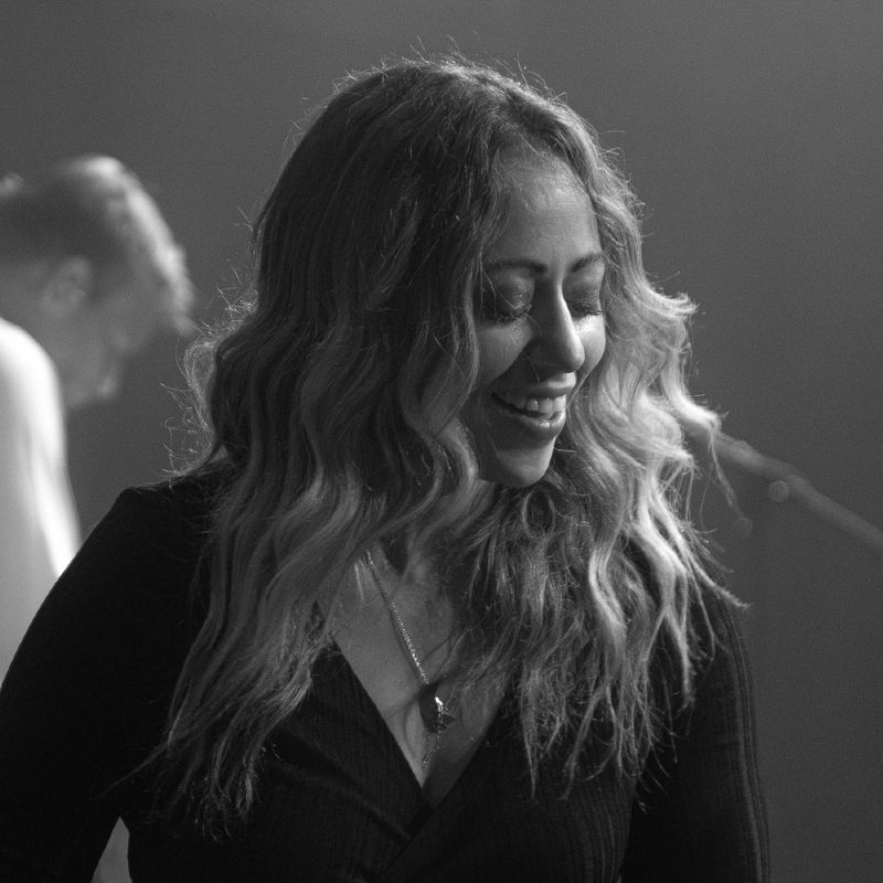 Rachel Waldman Francis performing as Stevie Nicks with Tell Me Lies - Fleetwood Mac Tribute Smiling woman with long, wavy hair wearing a dark top and necklace, onstage.