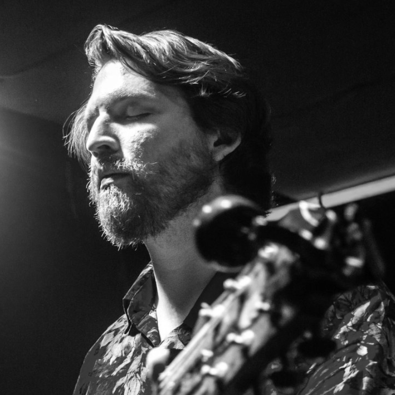 Sean Williams performing as Lindsey Buckingham with Tell Me Lies - Fleetwood Mac Tribute Man singing into a microphone, mouth open, smiling. Black and white close-up.