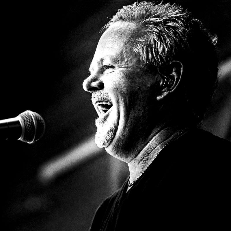 Tom Richards performing with Tell Me Lies - Fleetwood Mac Tribute Man singing into a microphone, smiling widely. Black and white photo.