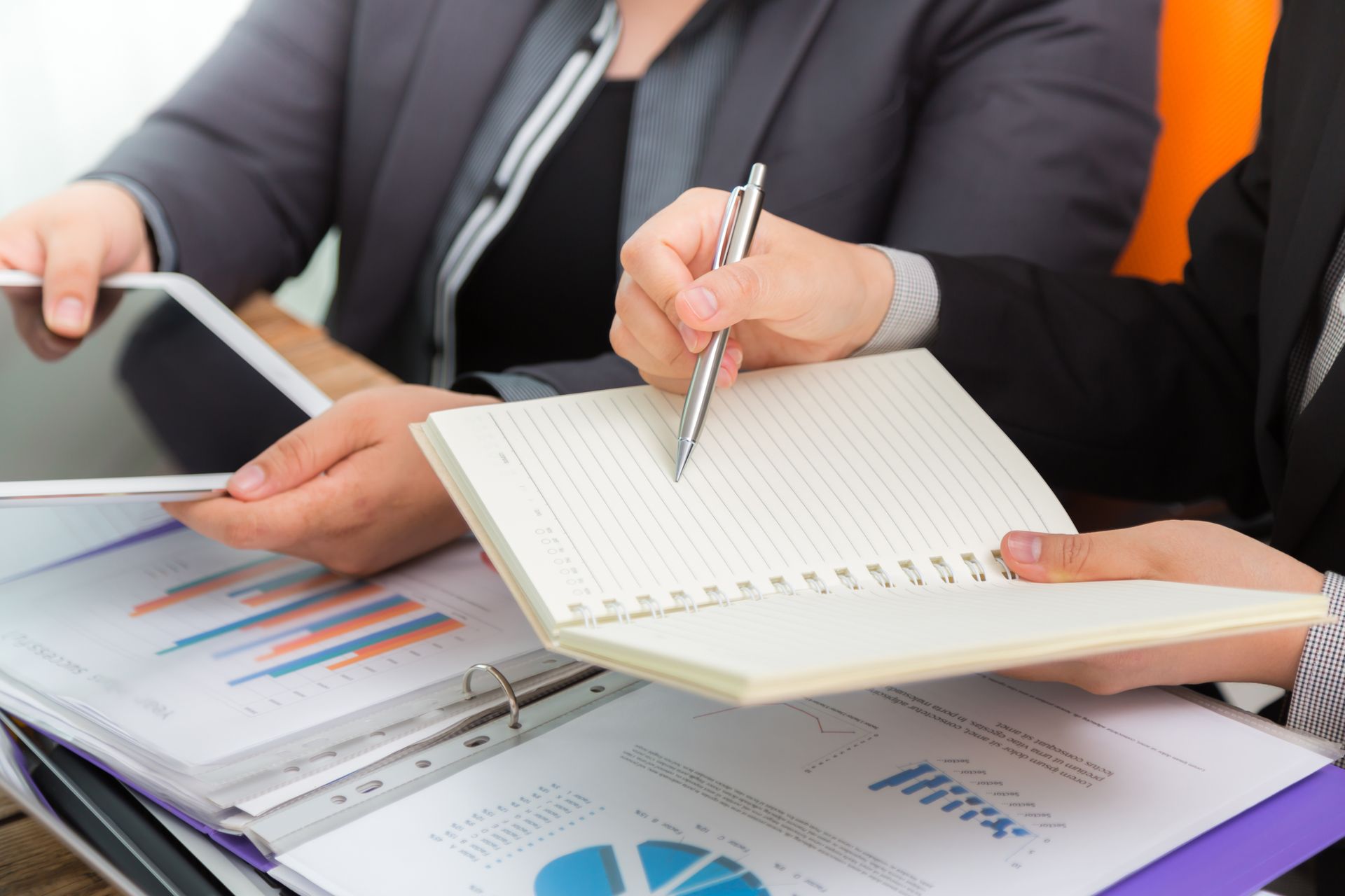 Gente de negocios analizando datos financieros con tableta y bloc de notas.