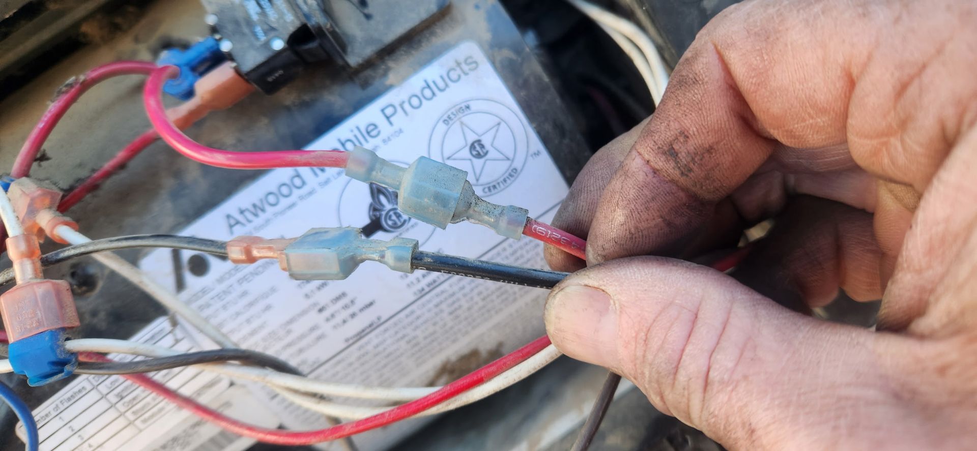 Close-up of dirty hands holding electrical wires and connectors over a motorcycle wiring diagram.