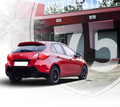 Red hatchback car parked in front of a building with a large
