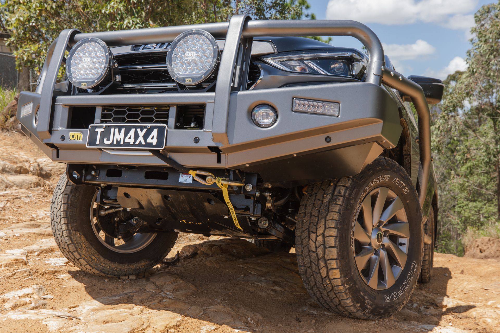 Gray off-road truck with a bull bar, spotlights, and winch driving on a dirt trail.