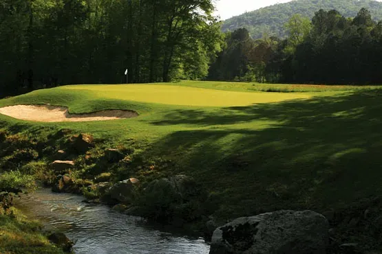 A golf course with a stream running through it and trees in the background.
