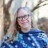 Smiling woman author with glasses and wavy hair wearing a blue patterned shawl outdoors