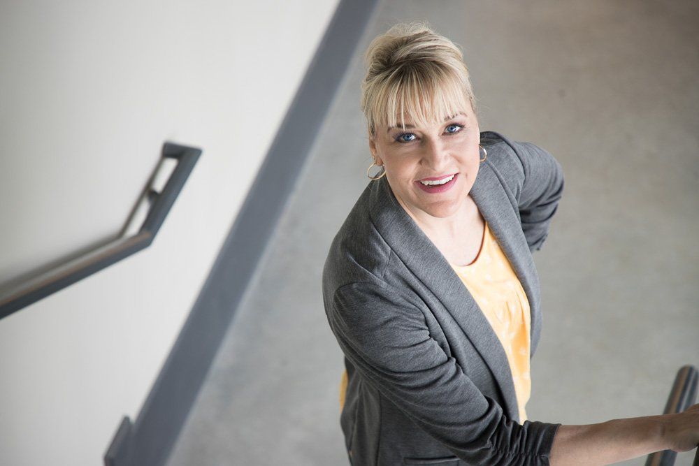 Smiling woman in a gray blazer standing on stairs and looking up at the camera