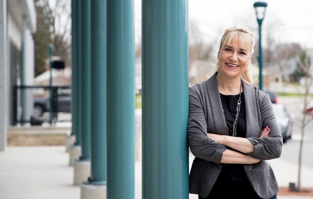 Smiling woman in a gray blazer leaning against teal columns on a sidewalk