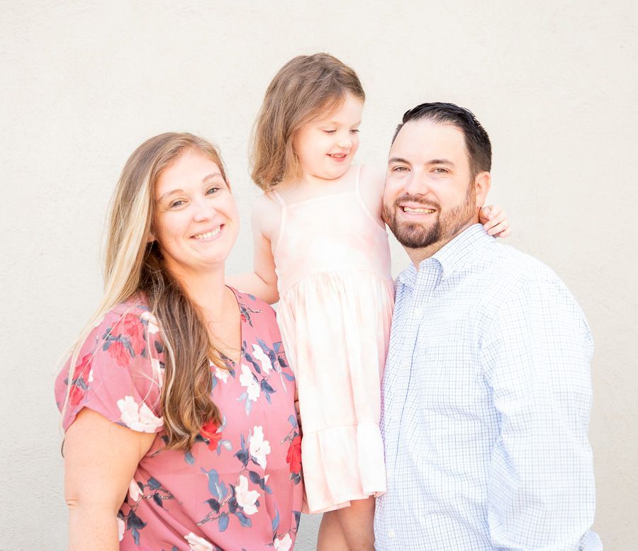 Smiling family of three standing together against a bright white background in Fishers.