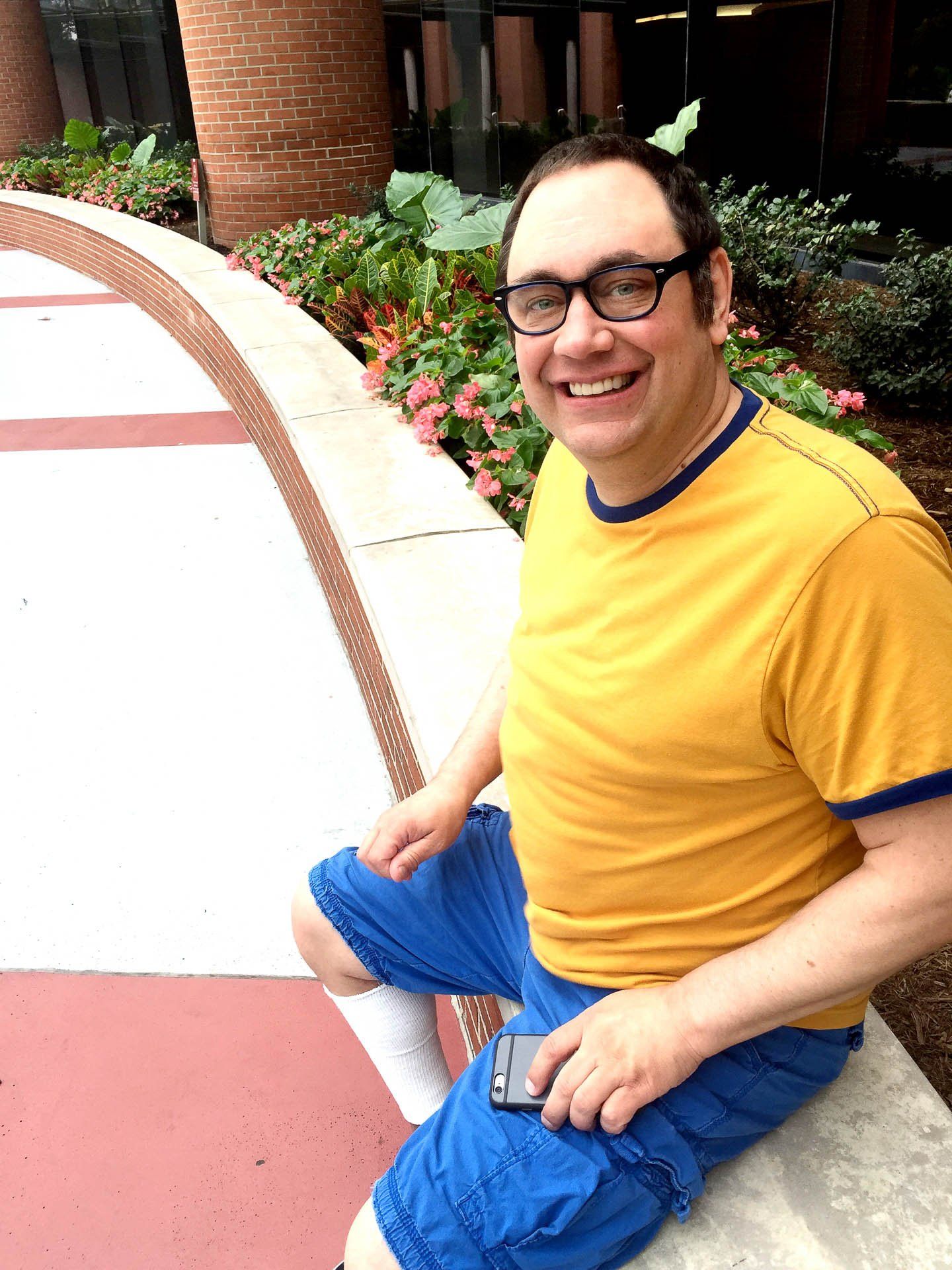 Smiling business coach in a yellow shirt and blue shorts sitting on a curb outdoors