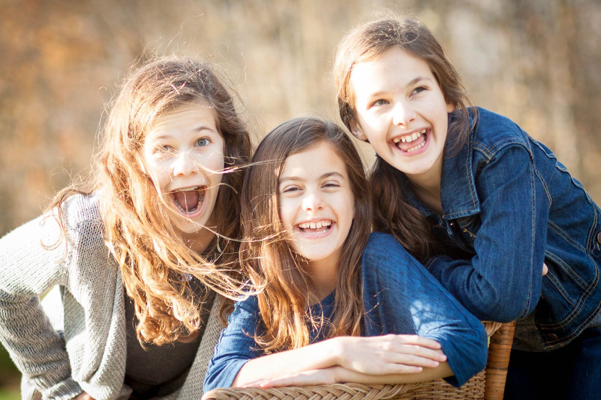 Three smiling sisters with happy faces leaning together outdoors in bright sunlight