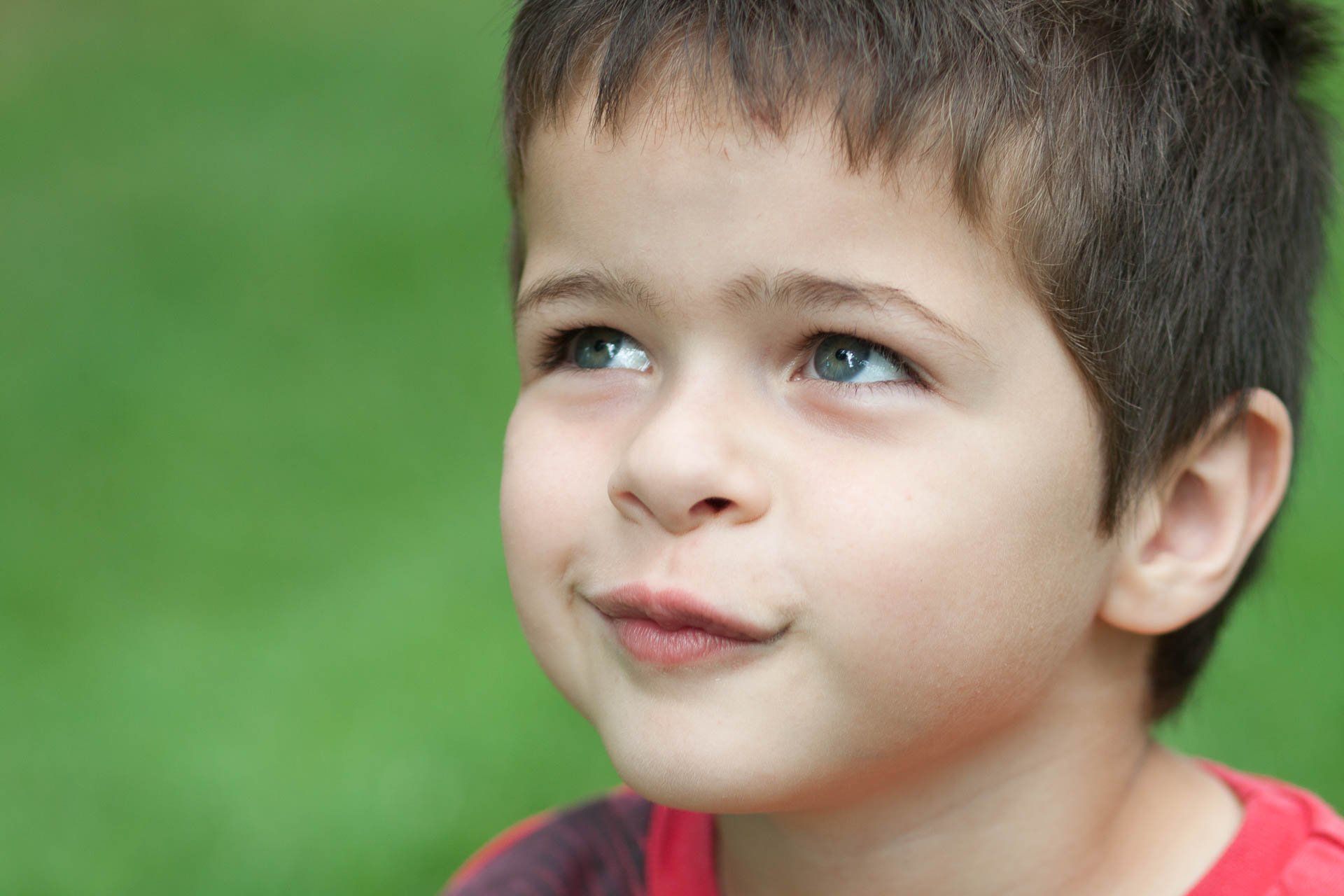 Close-up of a child with blue eyes looking upward, against a blurred green background in Indianapolis, Indiana