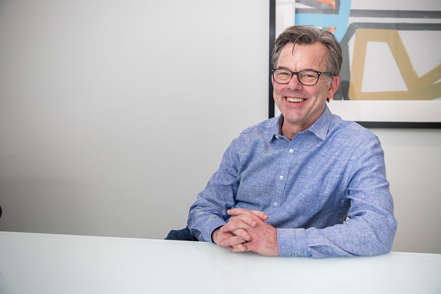 Smiling man in a blue shirt sitting at a white table in an office setting