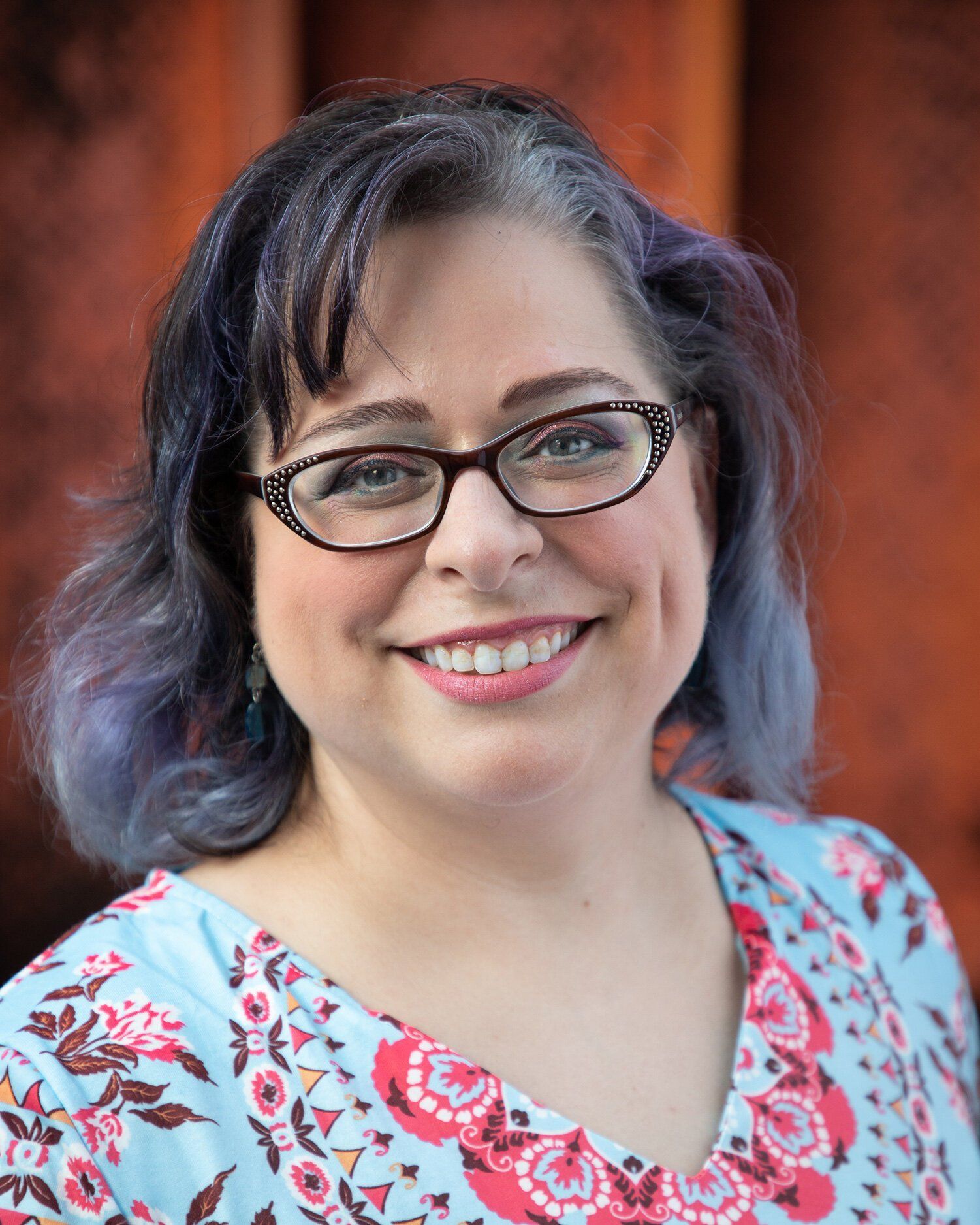 Headshot of a Zionsville Indiana woman with glasses and dark hair in a light blue top against a warm blurred background
