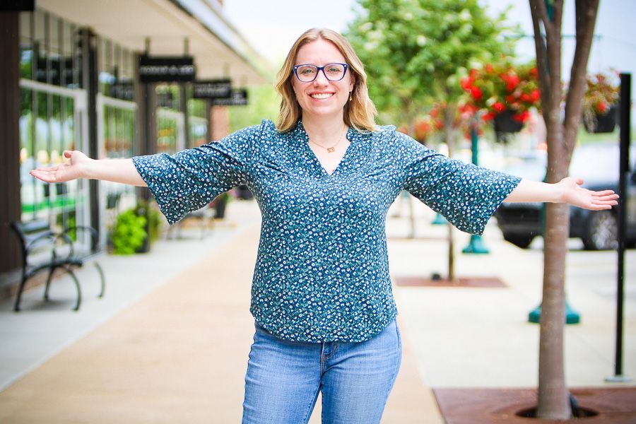 Marketing coach smiling with arms outstretched on a sidewalk near storefronts