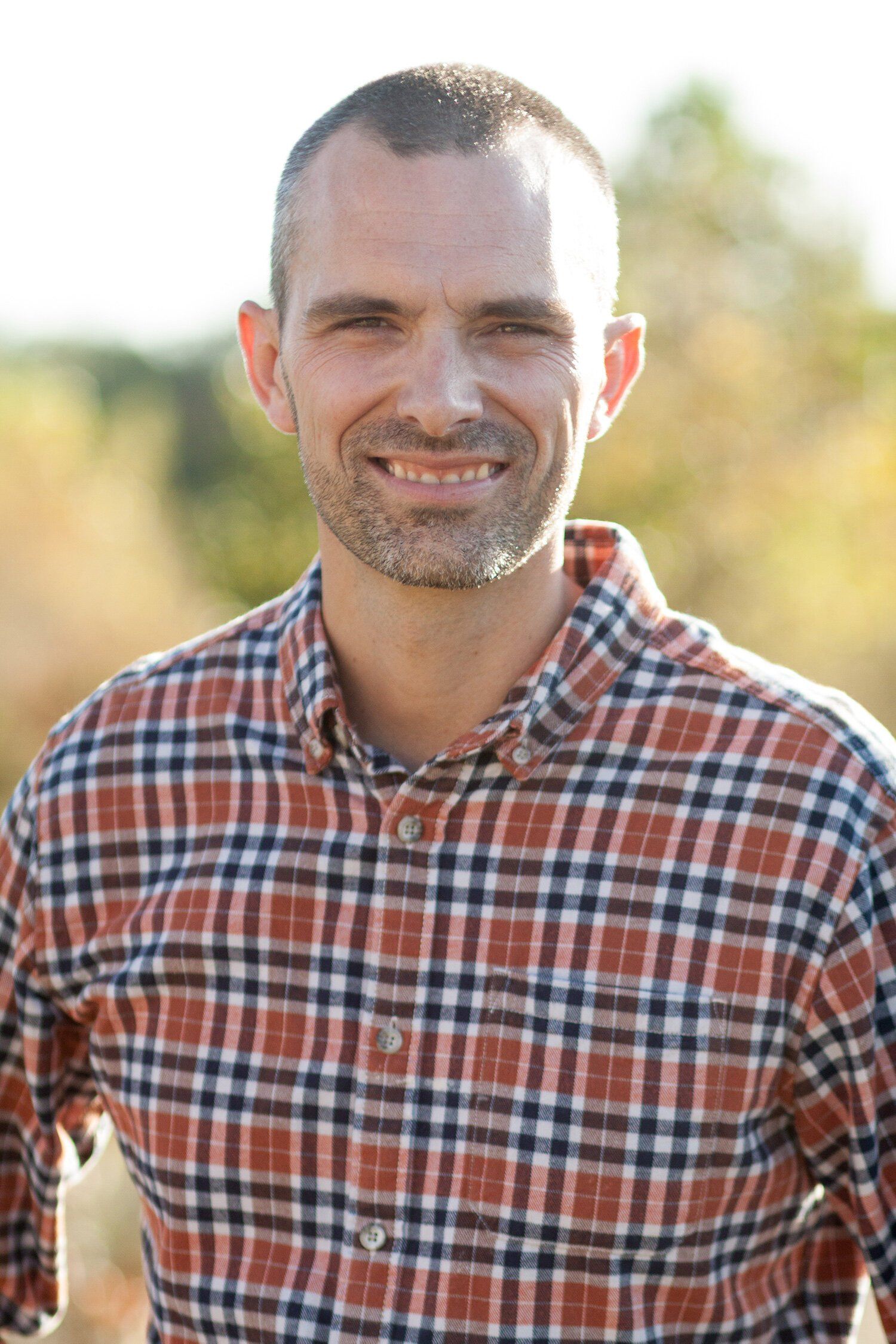 Headshot of a Pendleton Indiana man smiling in a red plaid shirt outdoors with a blurred background