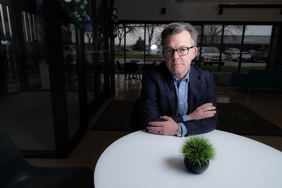 Indianapolis Business man seated at a round white table with arms crossed in a modern office lobby, small plant in foreground