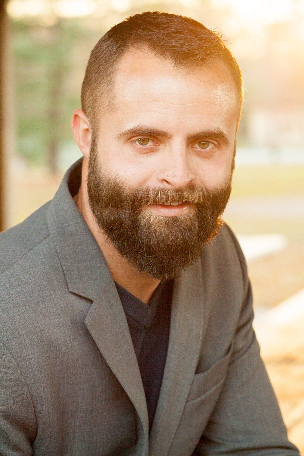 Headshot of a Fishers Indiana bearded man in a gray blazer smiling against a warm, blurred background