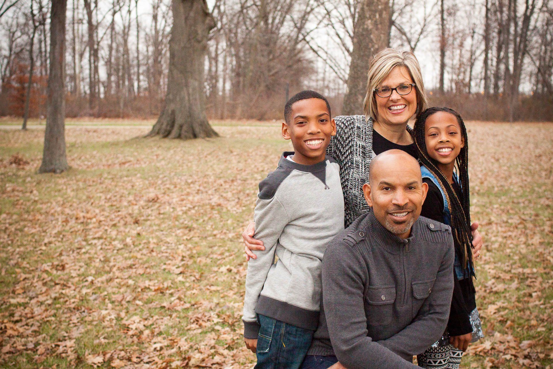 Four people smiling in a leaf-covered park, with trees in the background in Westfield, Indiana