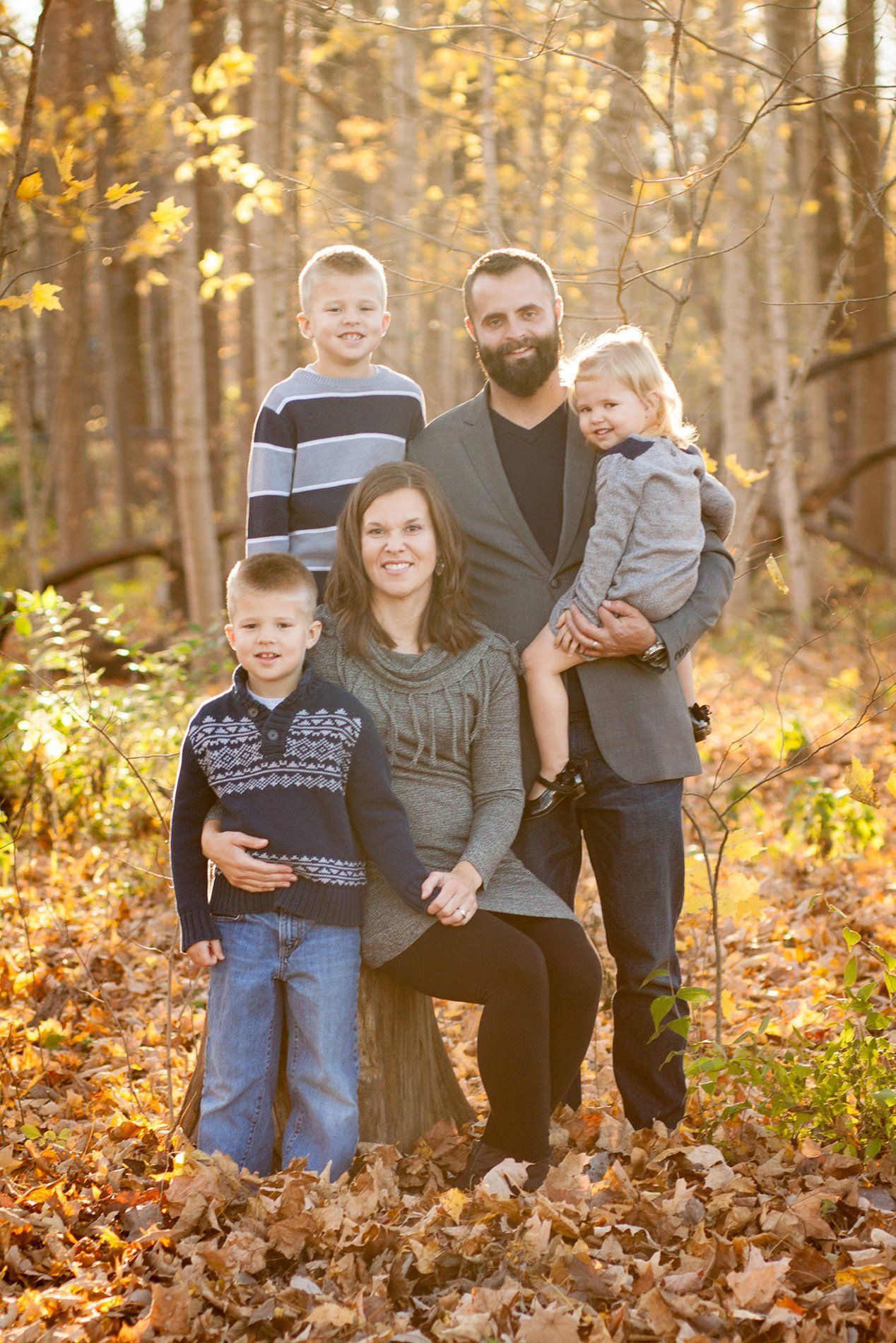 Family of five posing outdoors in Indianapolis autumn woods, with golden leaves and warm sunlight.