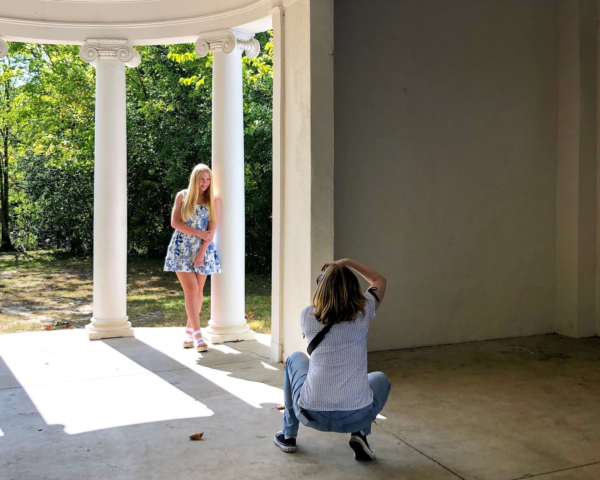 Photographer Kristin Madeja takes a picture of a senior girl in a sunlit colonnade.