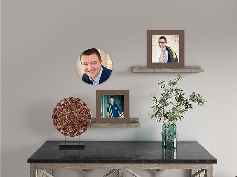 Floating shelves with framed photos of a high school senior boy, and a vase of greenery above a black console table