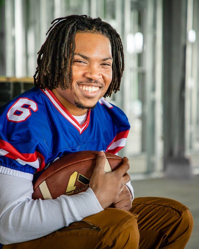 High school senior football player from Hamilton Southeastern High School in a blue jersey holding a football indoors.