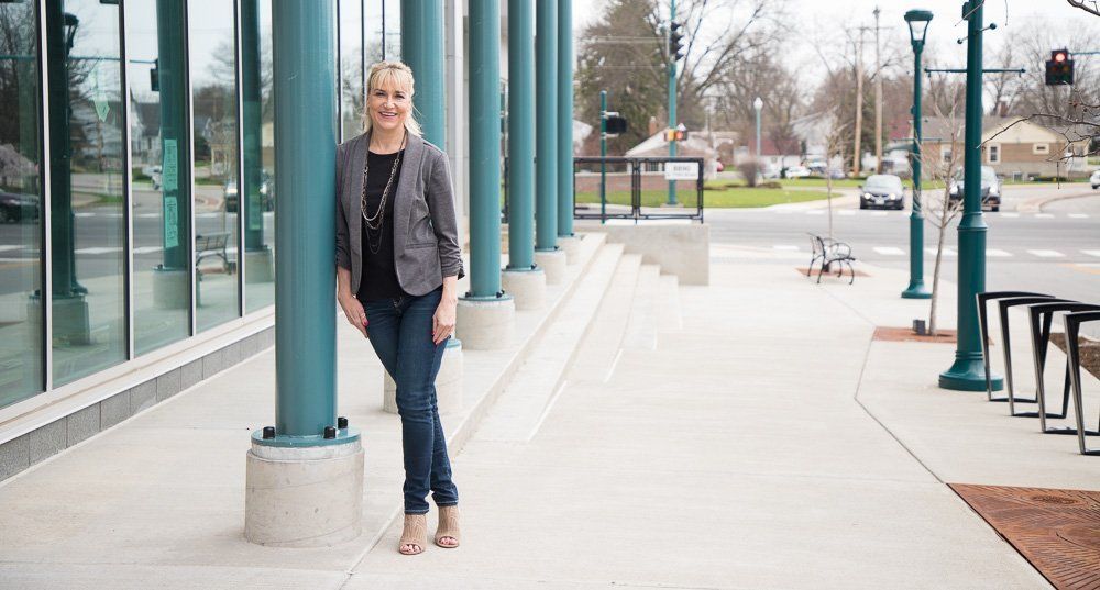 Woman leaning against a teal pillar outside a glass-front building on a sidewalk