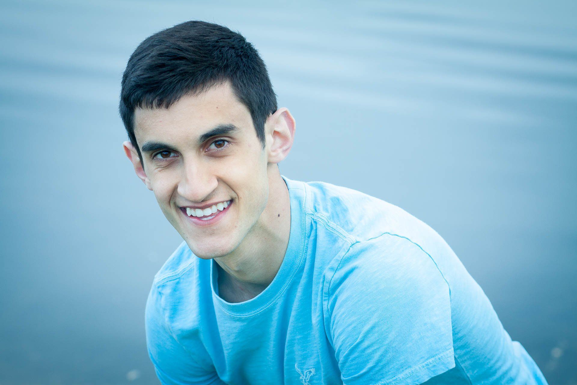 High School senior boy poses in a light blue shirt against a soft blue background