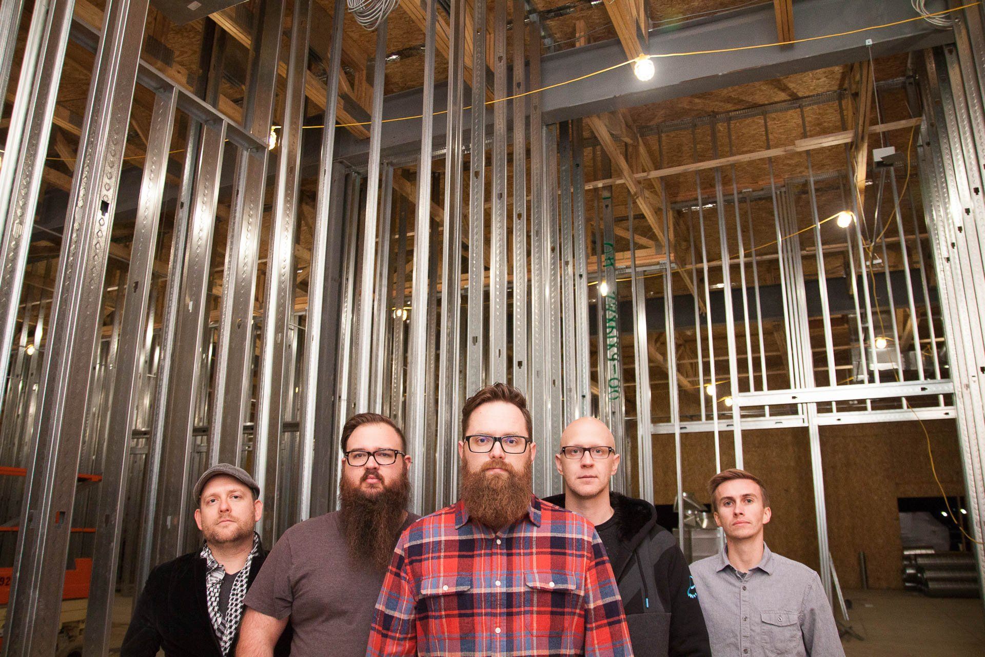 Five men standing in an unfinished building with exposed wood framing and metal studs
